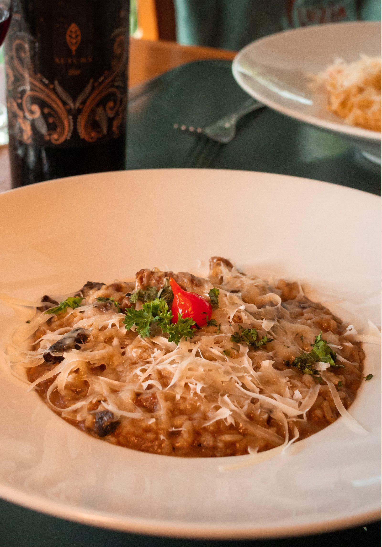 Risoto de filé mignon e funghi finalizado com lascas de parmesão e uma pimenta vermelha, ao lado de uma taça de vinho tinto