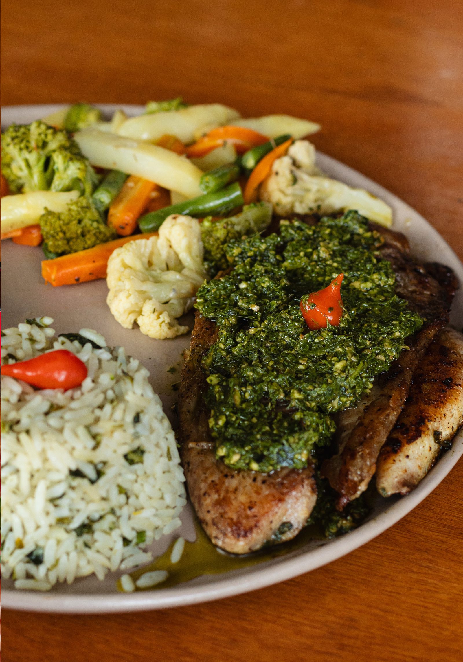 Filé de tilápia grelhado coberto de molho pesto, com arroz de ervas e seleta de legumes salteados